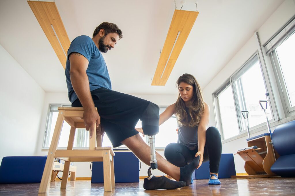 A trainer assists a man with a prosthetic leg during indoor physical therapy.