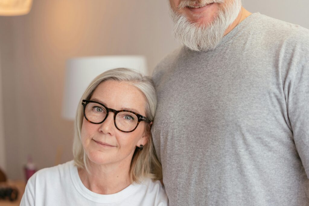 Happy senior couple smiling warmly in a cozy indoor setting, wearing casual attire.